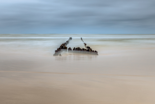 View of wooden breakwater remains on a sandy beach with misty long exposure water under an overcast sky in Debki Pomeranian Voivodeship Poland. View of wooden breakwater remains on a sandy beach with misty long exposure water under an overcast sky in Debki Pomeranian Voivodeship Poland.