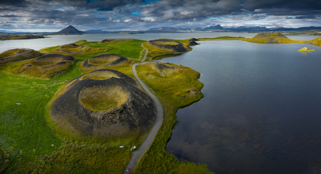 Aerial view of Skutustadagigar pseudocraters surrounded by green fields and the calm waters of Lake Myvatn under a cloudy sky Iceland.