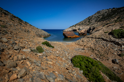 View of a rusted shipwreck resting in a secluded rocky cove under a clear night sky in Lefkada Greece.