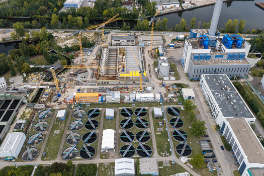 Aerial view of Klarwerk Ruhleben sewage treatment plant with circular sedimentation tanks industrial buildings and active construction cranes in Berlin Berlin Germany.