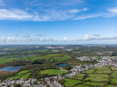 Aerial view of the lush green Cornish landscape with residential housing small lakes and the distant Meledor Clay pits under a bright blue sky in St Austell Cornwall United Kingdom. Aerial view of the lush green Cornish landscape with residential housing small lakes and the distant Meledor Clay pits under a bright blue sky in St Austell Cornwall United Kingdom.