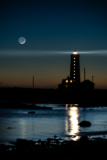 View of Grotta Lighthouse at night with a crescent moon in the dark sky and light reflecting on the water in Seltjarnarnes Seltjarnarnesbaer Iceland. View of Grotta Lighthouse at night with a crescent moon in the dark sky and light reflecting on the water in Seltjarnarnes Seltjarnarnesbaer Iceland.