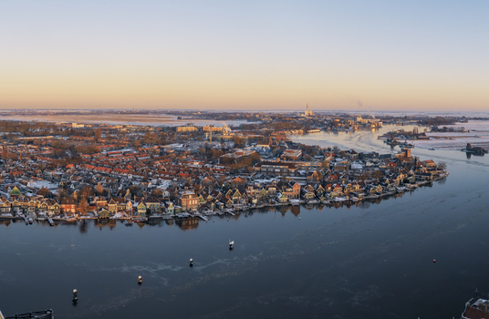 Aerial view of Zaanse Schans with historic windmills and traditional wooden houses along the Zaan river in winter with snow covered rooftops and golden light. Zaandam Noord Holland Netherlands. Aerial view of Zaanse Schans with historic windmills and traditional wooden houses along the Zaan river in winter with snow covered rooftops and golden light. Zaandam Noord Holland Netherlands.