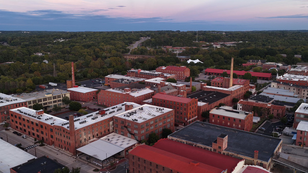 Aerial view of historic brick industrial buildings in the River District featuring red brick architecture tall chimneys and lush greenery under a sunset sky in Danville Virginia United States. Aerial view of historic brick industrial buildings in the River District featuring red brick architecture tall chimneys and lush greenery under a sunset sky in Danville Virginia United States.