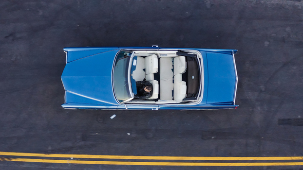 Aerial view of a blue vintage convertible car with a person sitting in the driver seat on an asphalt road with yellow markings in Los Angeles California United States. Aerial view of a blue vintage convertible car with a person sitting in the driver seat on an asphalt road with yellow markings in Los Angeles California United States.