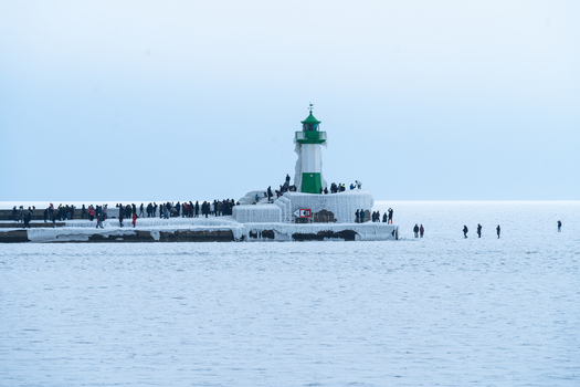 View of the ice covered Molenfeuer Sassnitz lighthouse on a frozen pier with people walking along the structure in Sassnitz Mecklenburg Vorpommern Germany.