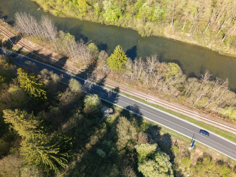 Aerial view of the Orava river flowing alongside a railway track and a road with a car passing through lush green forests Nizna Zilina Region Slovakia.