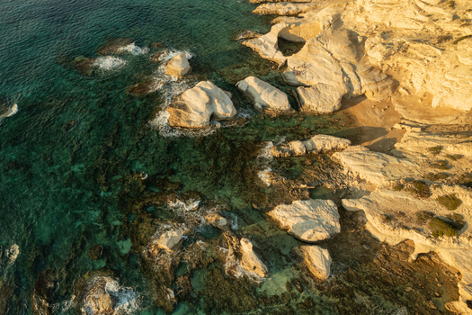 Aerial view of rugged coastline where the teal sea meets the sun baked rocks creating a striking contrast of colors and textures Thira Thira Greece. Aerial view of rugged coastline where the teal sea meets the sun baked rocks creating a striking contrast of colors and textures Thira Thira Greece.