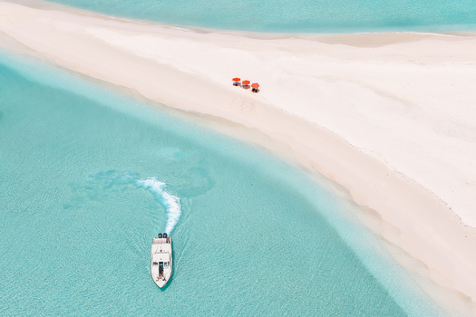 Aerial view of a pristine white sandbar surrounded by turquoise ocean water with a boat and red umbrellas Vashafaru Haa Alif Atoll Maldives. Aerial view of a pristine white sandbar surrounded by turquoise ocean water with a boat and red umbrellas Vashafaru Haa Alif Atoll Maldives.