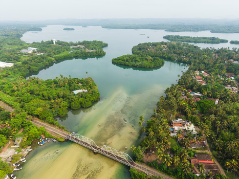 Aerial view of Koggala Lake featuring lush green islands and a white railway bridge crossing the water surrounded by tropical trees in Koggala Southern Province Sri Lanka. Aerial view of Koggala Lake featuring lush green islands and a white railway bridge crossing the water surrounded by tropical trees in Koggala Southern Province Sri Lanka.