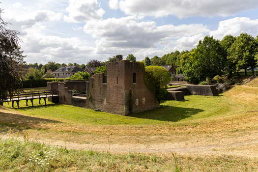 View of the historic brick ruins of Heusden Castle with a wooden footbridge crossing the grassy moat under a blue sky in Heusden North Brabant Netherlands.
