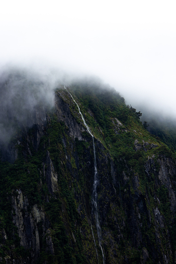 View of a powerful waterfall cascading down a steep rugged mountain shrouded in mist Milford Sound Southland Region New Zealand.