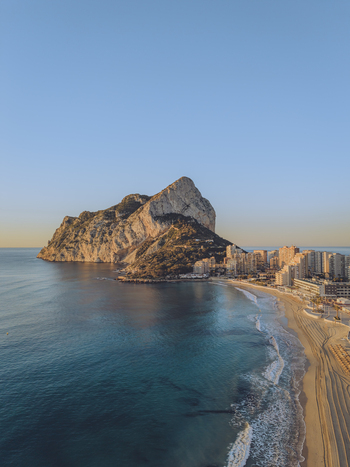 Aerial view of the Penyal d Ifac limestone rock formation rising from the Mediterranean Sea next to the sandy beach and coastal buildings in Calp Valencian Community Spain. Aerial view of the Penyal d Ifac limestone rock formation rising from the Mediterranean Sea next to the sandy beach and coastal buildings in Calp Valencian Community Spain.
