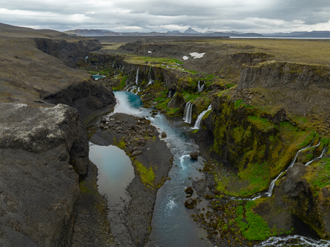 Aerial view of Sigoldugljufur canyon featuring vibrant blue water cascading waterfalls and lush moss covered volcanic cliffs under a cloudy sky in Rangarthing ytra Iceland. Aerial view of Sigoldugljufur canyon featuring vibrant blue water cascading waterfalls and lush moss covered volcanic cliffs under a cloudy sky in Rangarthing ytra Iceland.