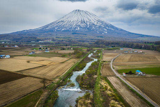 Aerial view of the snow capped Mount Yotei rising above the winding river and agricultural fields in the rural landscape of Niseko Hokkaido Japan.