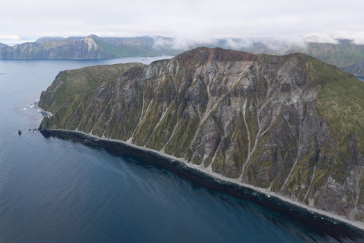 Aerial view of the rugged coastal cliffs and volcanic terrain of Unalaska featuring steep slopes rocky textures and the dark waters of the Bering Sea in Unalaska Alaska United States.