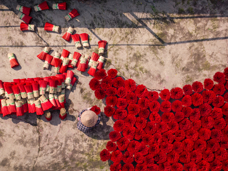 Aerial view of a worker wearing a conical hat arranging bundles of red incense sticks drying on the ground in Vietnam. Aerial view of a worker wearing a conical hat arranging bundles of red incense sticks drying on the ground in Vietnam.