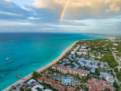 Aerial view of Grace Bay with its turquoise waters sandy beach and resort buildings under a rainbow in the sky Grace Bay Caicos Islands Turks and Caicos Islands. Aerial view of Grace Bay with its turquoise waters sandy beach and resort buildings under a rainbow in the sky Grace Bay Caicos Islands Turks and Caicos Islands.