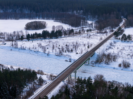 Aerial view of a bridge crossing a frozen river surrounded by snow covered fields and dense pine forests in Lithuania. Aerial view of a bridge crossing a frozen river surrounded by snow covered fields and dense pine forests in Lithuania.