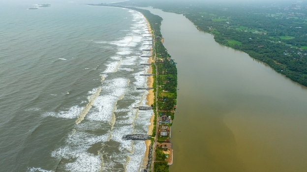 Aerial view of Mattu Beach with its narrow strip of land separating the Arabian Sea from the backwaters featuring stone breakwaters and lush palm trees Udupi Karnataka India.
