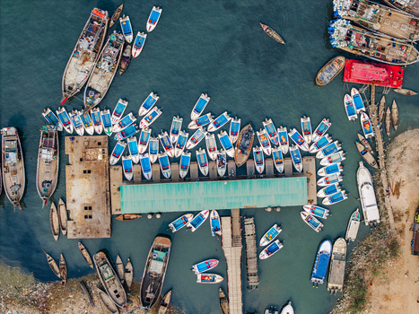 Moheskhali Upazila Bangladesh 11 March 2026 Aerial view of numerous small blue and white motorboats and larger wooden fishing vessels docked at a pier with a green roof and people on the decks. Moheskhali Upazila Bangladesh 11 March 2026 Aerial view of numerous small blue and white motorboats and larger wooden fishing vessels docked at a pier with a green roof and people on the decks.