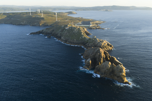 Aerial view of the rocky coastline and the historic Torre de Hercules lighthouse surrounded by the Atlantic Ocean with wind turbines on the distant hills in Galicia Spain.