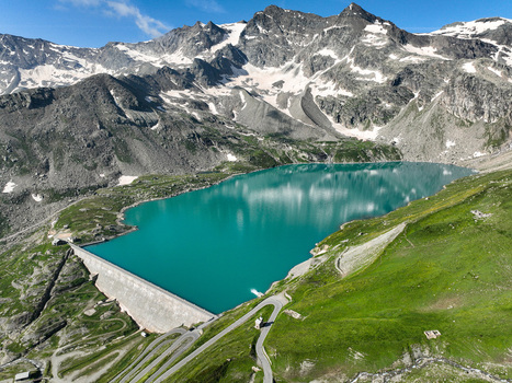 Aerial view of Serru Lake with its turquoise water massive concrete dam winding mountain roads and snow dusted peaks under a clear sky Ceresole Reale Piedmont Italy. Aerial view of Serru Lake with its turquoise water massive concrete dam winding mountain roads and snow dusted peaks under a clear sky Ceresole Reale Piedmont Italy.