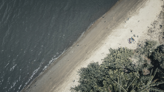 Aerial view of the tranquil shoreline where dark rippling water meets a sandy beach bordered by lush tropical greenery Badagry Lagos Nigeria.