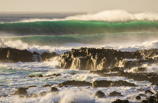 View of powerful ocean waves crashing against dark volcanic rocks along the coastline during golden hour at the North Shore in Haleiwa Hawaii United States.