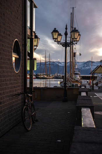 View of a bicycle parked by a brick wall near a vintage lamppost overlooking sailboats in the tranquil harbor against a backdrop of snow capped mountains Húsavík Iceland. View of a bicycle parked by a brick wall near a vintage lamppost overlooking sailboats in the tranquil harbor against a backdrop of snow capped mountains Húsavík Iceland.