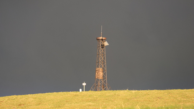 Aerial view of Le Colomby de Gex lattice tower standing on a grassy mountain ridge under a dark dramatic sky Echenevex Auvergne Rhone Alpes France. Aerial view of Le Colomby de Gex lattice tower standing on a grassy mountain ridge under a dark dramatic sky Echenevex Auvergne Rhone Alpes France.