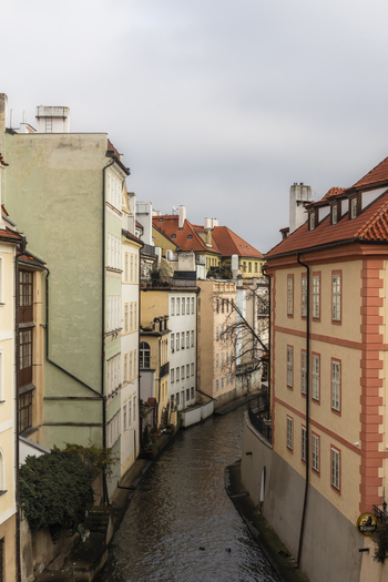 View of the Certovka canal flowing between historic pastel colored buildings with red tiled roofs under an overcast sky in Prague Prague Czechia. View of the Certovka canal flowing between historic pastel colored buildings with red tiled roofs under an overcast sky in Prague Prague Czechia.