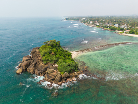 Aerial view of Devil s Rock a lush rocky outcrop surrounded by turquoise Indian Ocean waters and the tropical coastline Ahangama Southern Province Sri Lanka. Aerial view of Devil s Rock a lush rocky outcrop surrounded by turquoise Indian Ocean waters and the tropical coastline Ahangama Southern Province Sri Lanka.