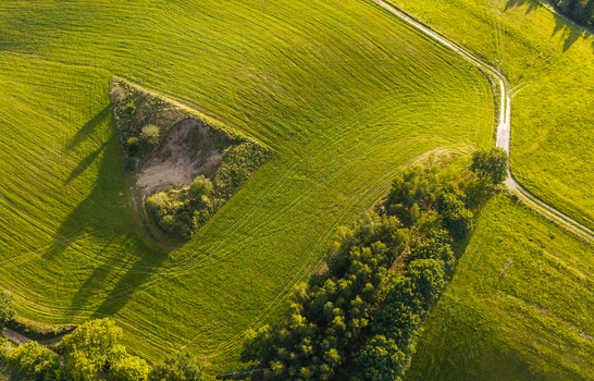 Aerial view of the Kashubia region featuring a triangular depression in a green field a dirt path and a line of trees in Pomeranian Voivodeship Poland. Aerial view of the Kashubia region featuring a triangular depression in a green field a dirt path and a line of trees in Pomeranian Voivodeship Poland.