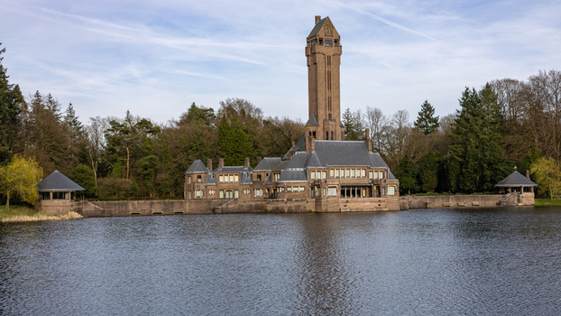 View of the Country Residence Museum Jachthuis Sint Hubertus featuring its tall brick tower and reflection on the water surface in Hoenderloo Gelderland Netherlands.