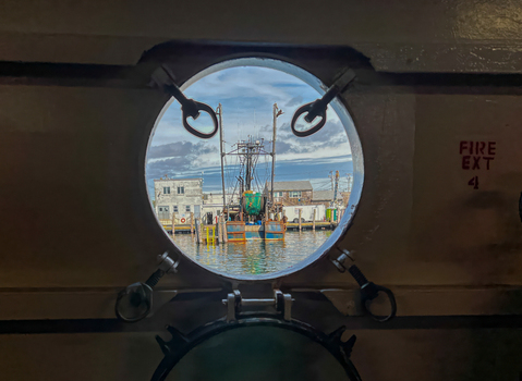 View of a fishing boat docked in the harbor seen through a circular ship porthole under a cloudy sky in Edgartown Massachusetts United States.