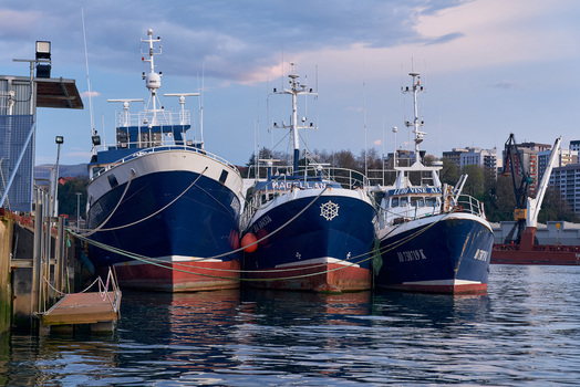 Pasai Donibane Spain 09 March 2026 View of three large blue fishing boats docked at Puerto Pasajes with industrial cranes and city buildings in the background under a soft evening sky. Pasai Donibane Spain 09 March 2026 View of three large blue fishing boats docked at Puerto Pasajes with industrial cranes and city buildings in the background under a soft evening sky.