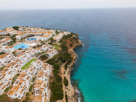 Aerial view of the coastal resort featuring white buildings swimming pools and rugged cliffs overlooking the turquoise Mediterranean sea in Cala Mendia Illes Balears Spain. Aerial view of the coastal resort featuring white buildings swimming pools and rugged cliffs overlooking the turquoise Mediterranean sea in Cala Mendia Illes Balears Spain.