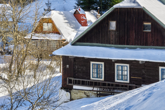 View of snow dusted wooden cabins their windows casting soft light nestled amidst a serene winter landscape inviting warmth against the crisp cold air Moce Slovakia.
