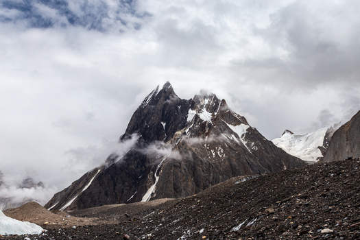 View of the rugged Baltoro Glacier surrounded by snow capped mountain peaks and rocky moraine under a cloudy sky in Baltoro Gilgit Baltistan Pakistan.
