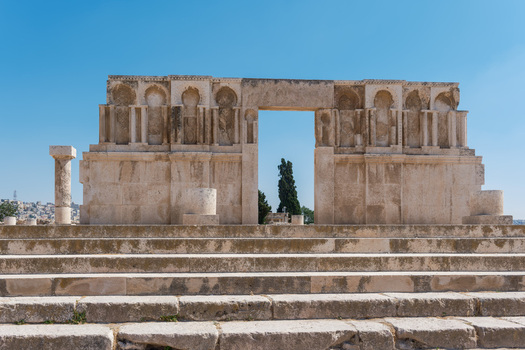 View of the Umayyad Palace ruins featuring an ornate stone gateway with intricate carvings under a clear blue sky in Amman Amman Governorate Jordan.