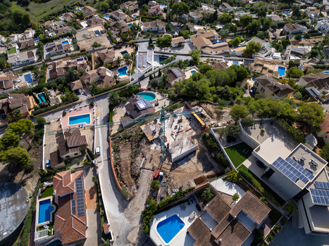 Aerial view of a construction site with a crane surrounded by residential villas swimming pools and Mediterranean vegetation in Moraira Valencian Community Spain.