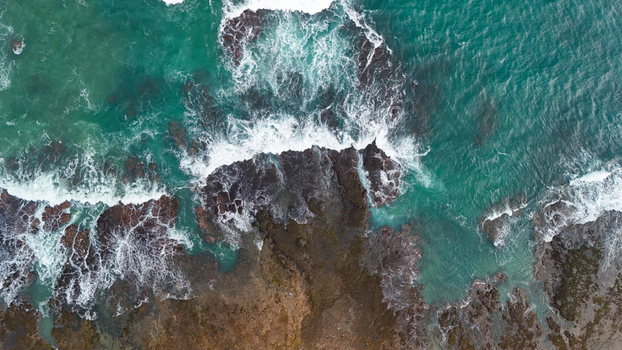 Aerial view of the rocky coastline with crashing waves and turquoise water in Indonesia.