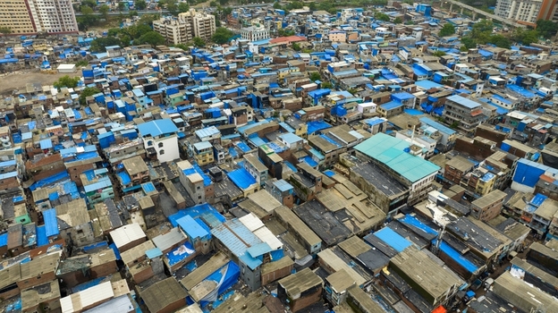 Aerial view of the dense urban landscape of Dharavi Slums with characteristic blue tarpaulin roofs and narrow alleyways in Mumbai Maharashtra India. Aerial view of the dense urban landscape of Dharavi Slums with characteristic blue tarpaulin roofs and narrow alleyways in Mumbai Maharashtra India.
