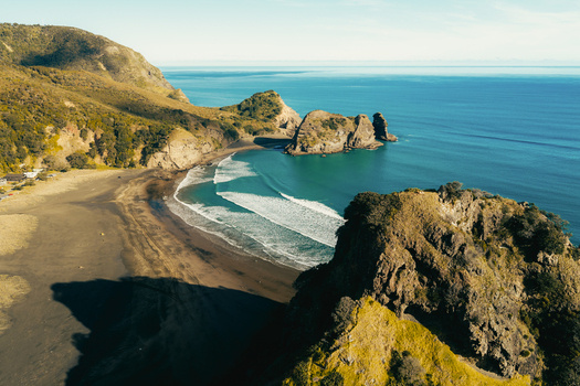 Aerial view of Piha Beach with its iconic black sand dramatic rock formations and rolling surf along the coastline in Auckland New Zealand. Aerial view of Piha Beach with its iconic black sand dramatic rock formations and rolling surf along the coastline in Auckland New Zealand.