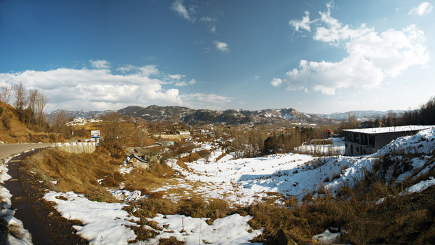 View of the snow covered mountainous landscape with dry grass distant peaks and a building under a clear blue sky in Rawalakot Kashmir Pakistan.