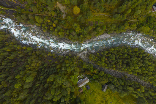 Aerial view of a turquoise river flowing through a dense green forest with small wooden cabins Fjaera Vestland Norway. Aerial view of a turquoise river flowing through a dense green forest with small wooden cabins Fjaera Vestland Norway.