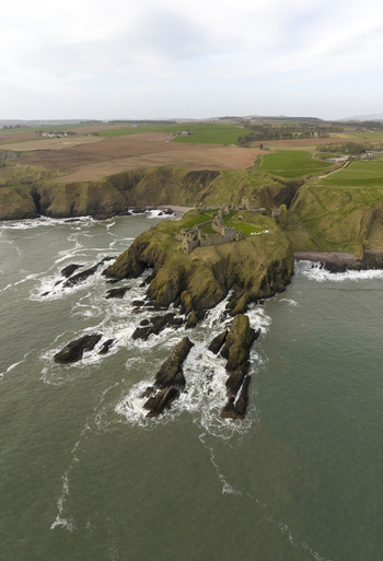 Aerial view of the medieval ruins of Dunnottar Castle perched on a rocky headland surrounded by the North Sea and steep cliffs in Stonehaven Scotland United Kingdom. Aerial view of the medieval ruins of Dunnottar Castle perched on a rocky headland surrounded by the North Sea and steep cliffs in Stonehaven Scotland United Kingdom.