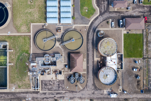 Aerial view of the wastewater treatment plant featuring circular sedimentation tanks industrial buildings and paved access roads in Woodburn Oregon United States. Aerial view of the wastewater treatment plant featuring circular sedimentation tanks industrial buildings and paved access roads in Woodburn Oregon United States.