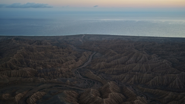 Aerial view of the rugged arid landscape of Issyk Kul leading to the vast lake under a twilight sky Issyk Kul Region Kyrgyzstan. Aerial view of the rugged arid landscape of Issyk Kul leading to the vast lake under a twilight sky Issyk Kul Region Kyrgyzstan.